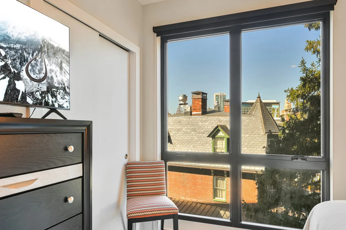 The image offers a contemporary living space with a comfortable chair, a television, and a large window overlooking the city skyline. The view through the window hints at the convenience of city living and the ability to unwind after a day of adventures.