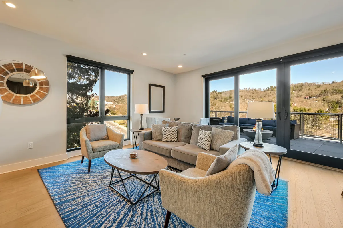 A comfortable seating area with a sofa and rug positioned near large windows and a coffee table. The scene feels intimate and inviting, perfect for curling up with a book or enjoying the sunset through the windows.