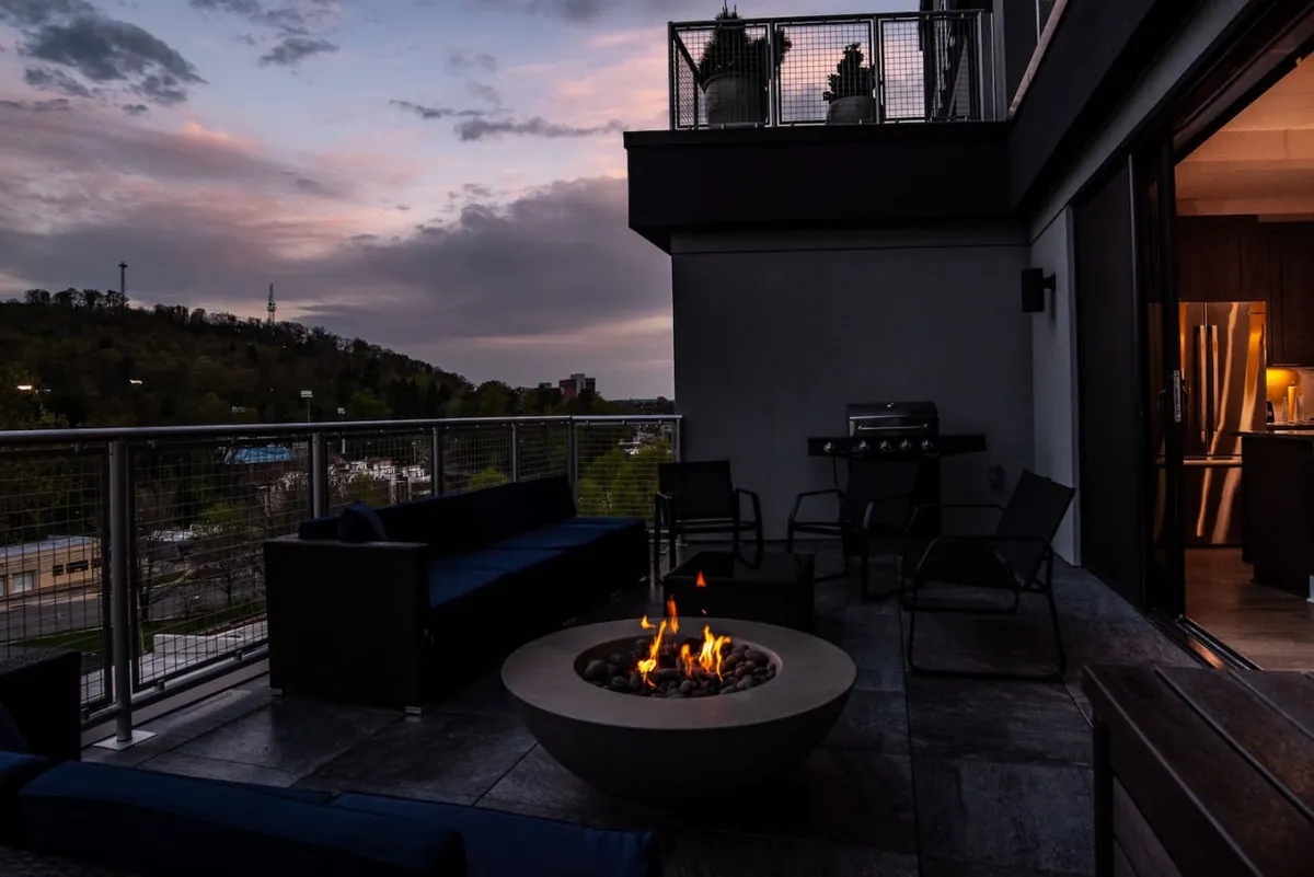 An exterior scene depicting an outdoor seating area with a fire pit and grill, set against a scenic landscape. The setup invites alfresco dining, socializing, and enjoying sunset views, perfectly capturing the balcony dining experience mentioned in the section.