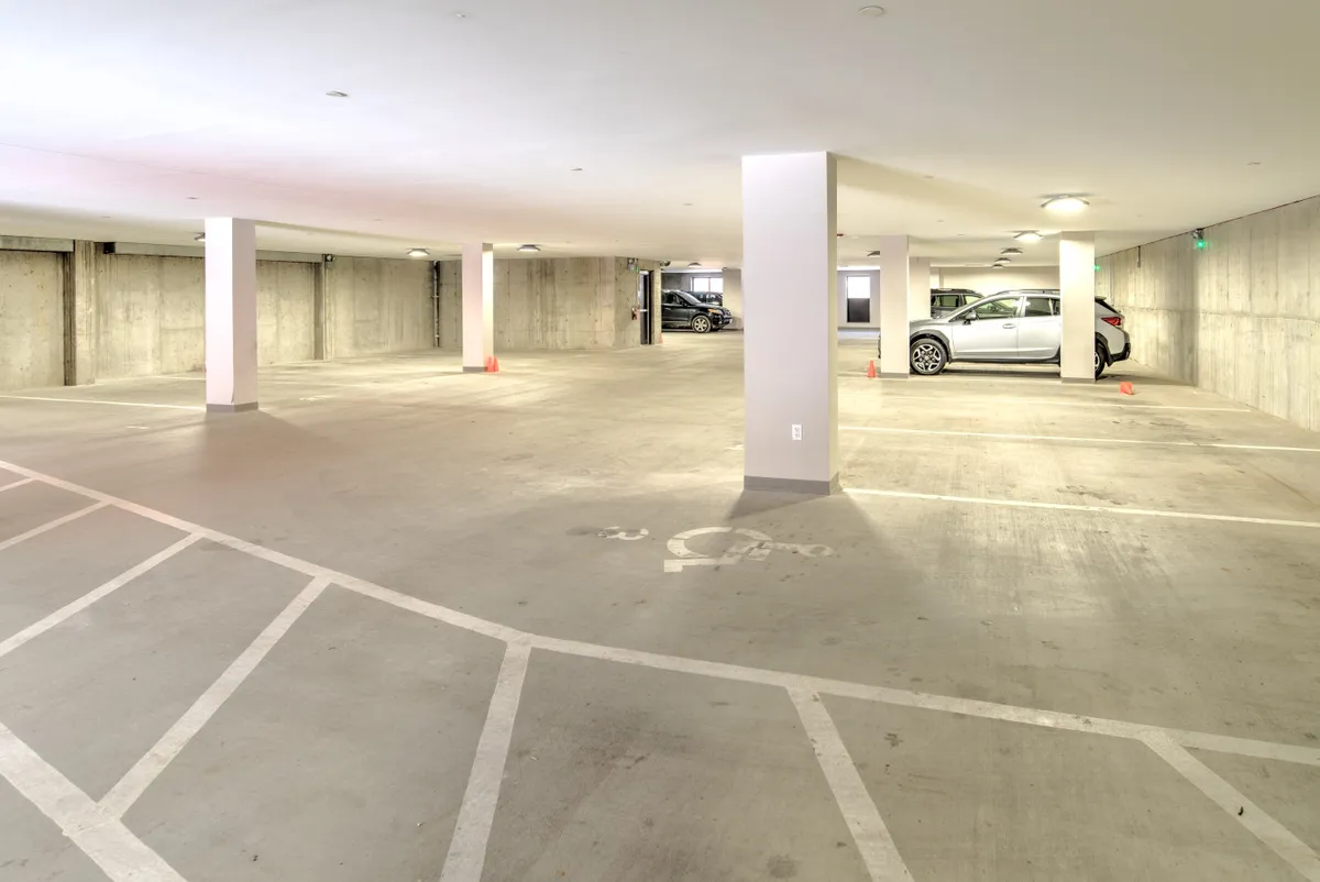 An interior view of the building’s parking area, featuring several marked parking spaces, vehicles of various sizes, and sturdy support columns. The lighting is practical, and the environment is clean and organized, highlighting the convenience and accessibility of onsite parking.