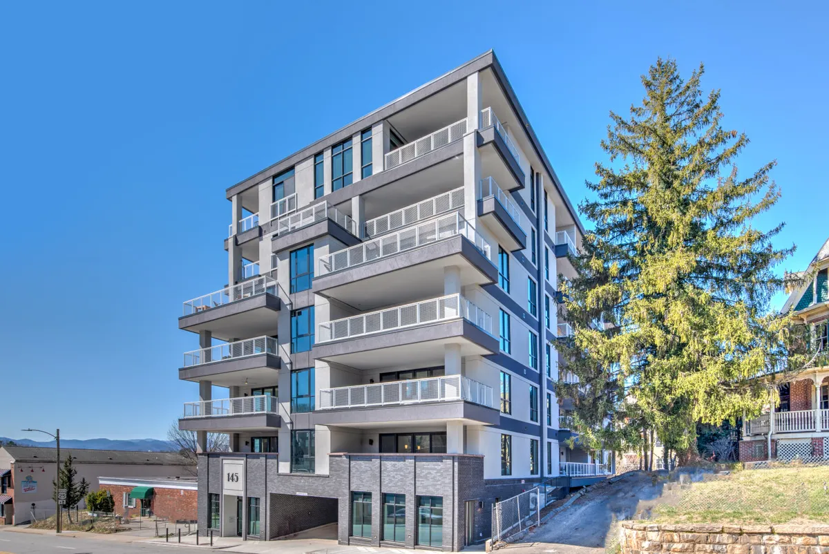 The modern exterior of the building highlights private balconies, large windows, and lush surrounding greenery. The scene captures the urban setting while hinting at the panoramic views residents enjoy from their own outdoor spaces.