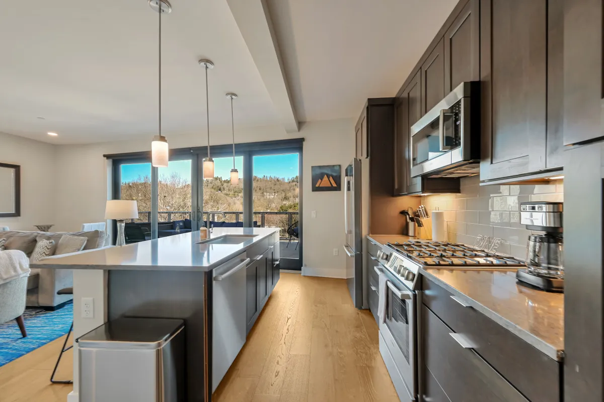 This image features a spacious, modern kitchen with a central island, stainless steel appliances, and expansive panoramic windows allowing in abundant natural light. The setting is inviting and seems perfect for both meal preparation and casual gatherings, with the views creating an inspiring backdrop for culinary adventures.