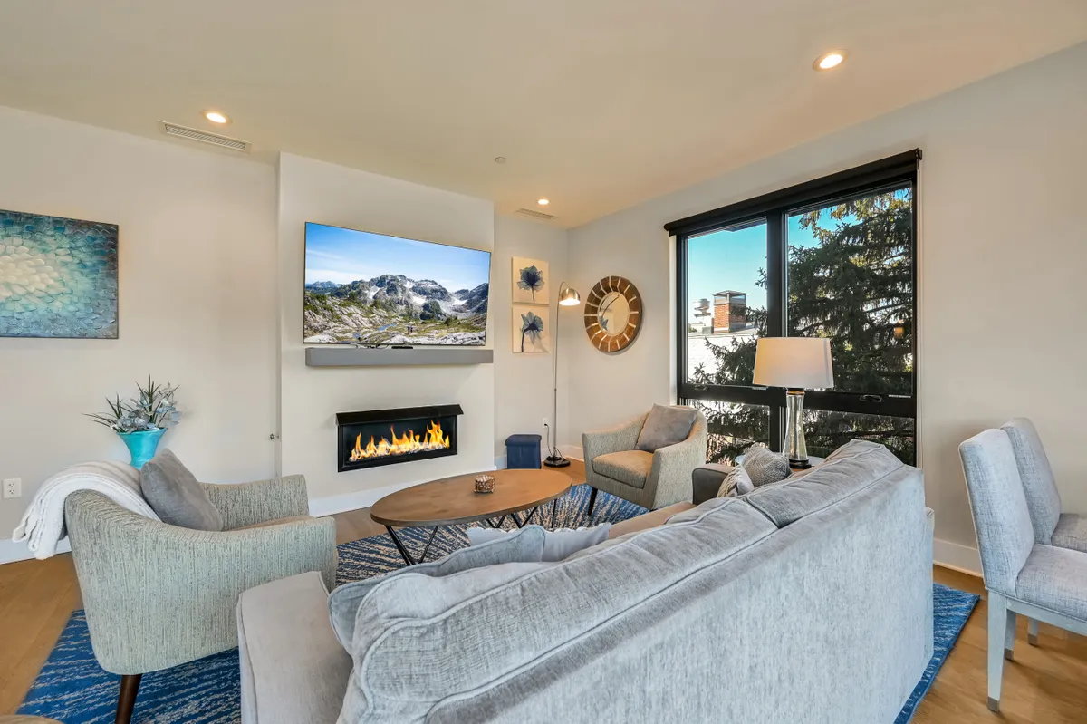 This image captures the heart of the living room, featuring a plush sofa oriented toward a glowing fireplace, with a coffee table in the center and a window offering views of the outdoors. Soft, ambient lighting and serene décor create an atmosphere ideal for relaxation or gathering with loved ones.